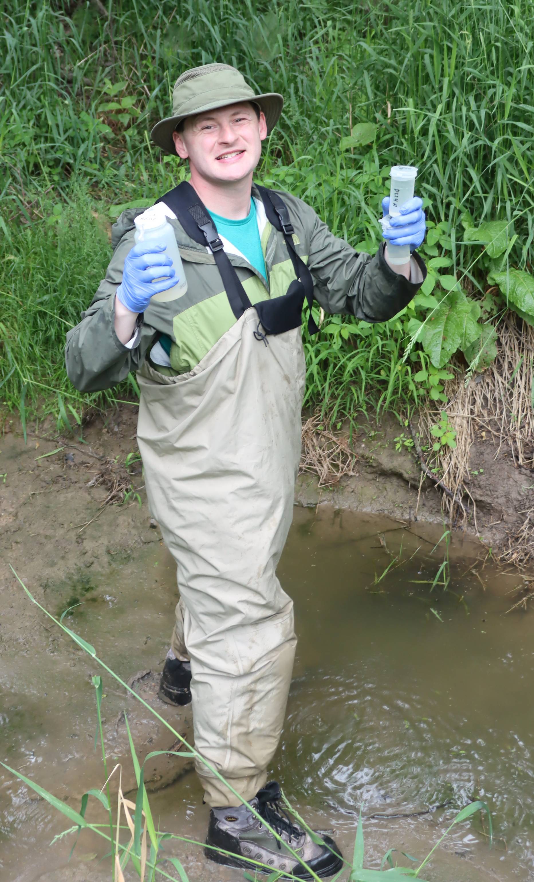 John Hart stands in a creek and displays water samples.